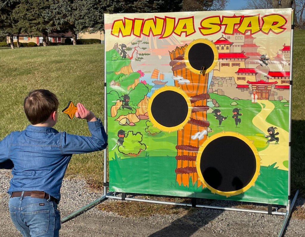 A young boy tosses a ninja star at the 7 by 7 ninjitsu background with velcro target receptors.